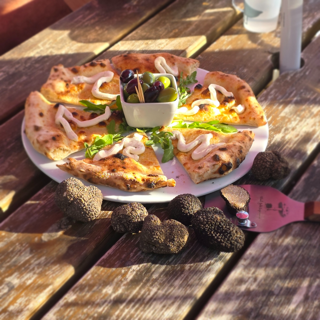 Truffle pizza platter served outdoors surrounded by fresh black truffles