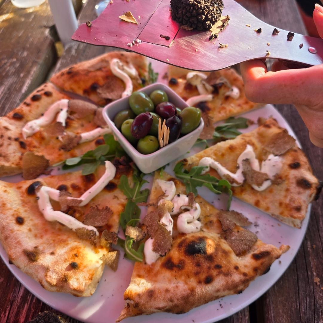 Fresh black truffle shaved over sliced pizza with rocket, olives and mascarpone