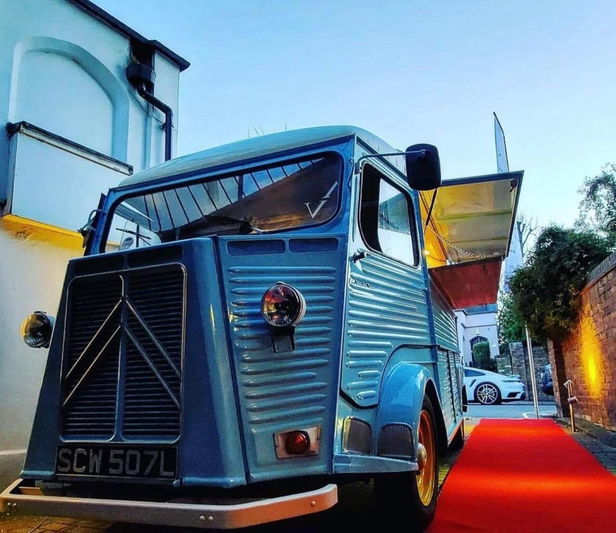 The Pizza On The Go vintage blue van arriving on a red carpet at an evening event
